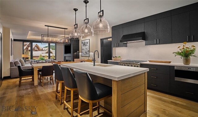 824 Settlement Trl Unit 31A, Big Sky, MT 59716 - kitchen featuring hanging light fixtures, a kitchen island with sink, a sink, wall chimney range hood, and dark cabinetry