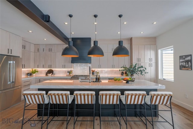 kitchen featuring an island with sink, high end refrigerator, pendant lighting, and light countertops