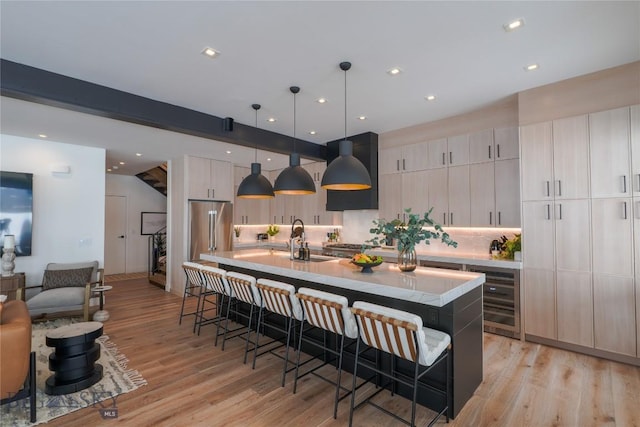 kitchen with an island with sink, high quality fridge, hanging light fixtures, extractor fan, and light countertops