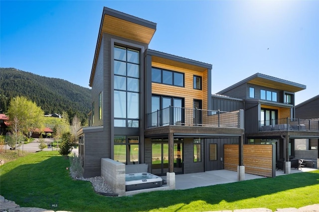 rear view of property with a balcony, a yard, a patio area, a mountain view, and board and batten siding