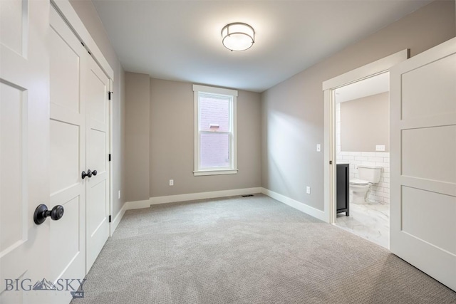 unfurnished bedroom with light carpet, visible vents, baseboards, ensuite bathroom, and a closet