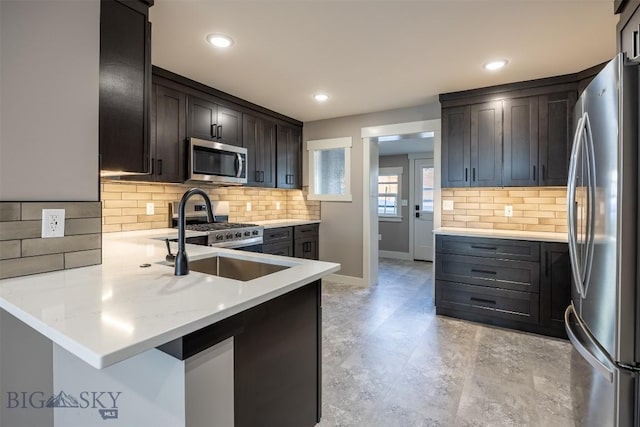 kitchen with dark brown cabinetry, baseboards, appliances with stainless steel finishes, a peninsula, and a sink