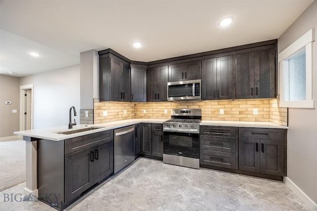 kitchen with dark brown cabinetry, a peninsula, a sink, light countertops, and appliances with stainless steel finishes