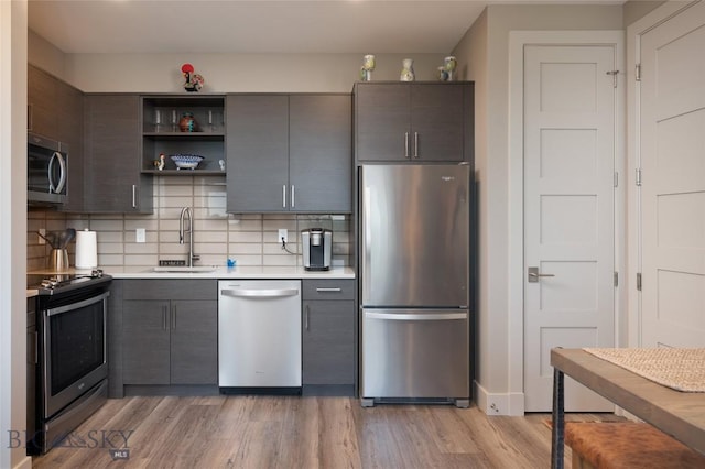 kitchen featuring light wood finished floors, open shelves, stainless steel appliances, light countertops, and a sink