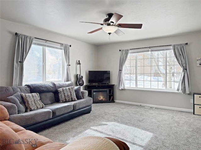 carpeted living area with a glass covered fireplace, a ceiling fan, and baseboards