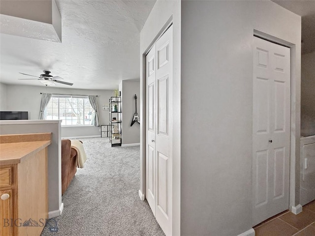 hall featuring a textured ceiling, carpet, and baseboards