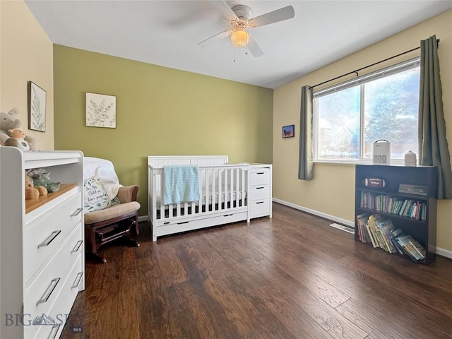 bedroom featuring dark wood finished floors, visible vents, a ceiling fan, a crib, and baseboards