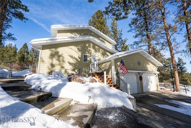 view of snow covered exterior featuring a garage and fence