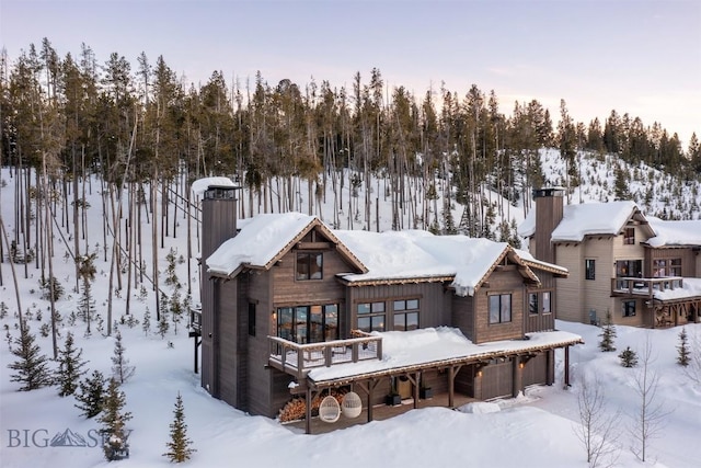 snow covered house with a garage and a chimney