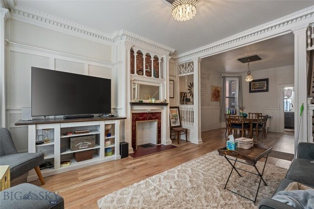 living area featuring a wainscoted wall, a tiled fireplace, wood finished floors, and ornate columns