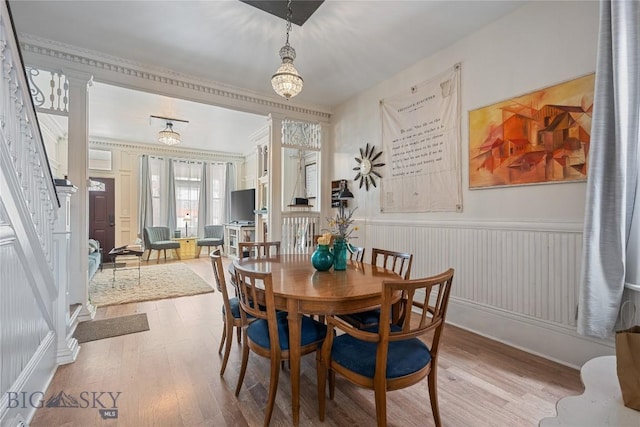 dining space with stairs, a wainscoted wall, decorative columns, and wood finished floors