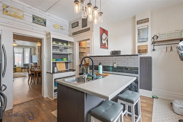 kitchen with dark wood finished floors, a kitchen breakfast bar, decorative light fixtures, a kitchen island with sink, and a sink