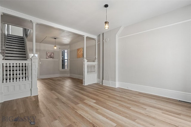 interior space featuring decorative columns, visible vents, stairway, light wood-type flooring, and baseboards