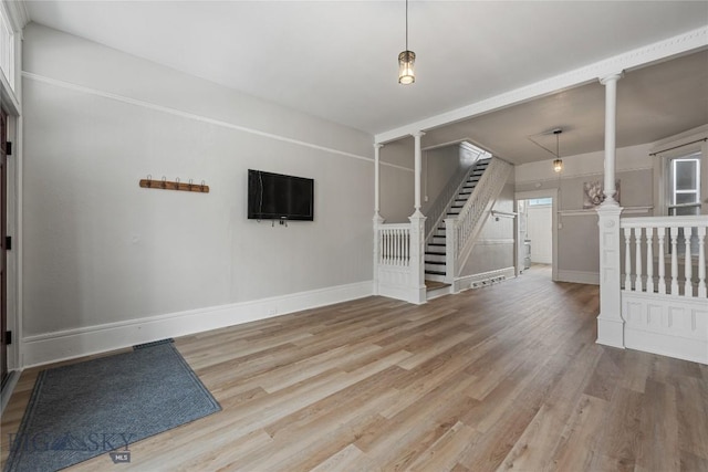 interior space with light wood-style flooring, baseboards, stairway, and ornate columns