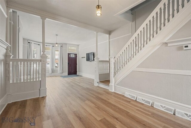 entrance foyer with ornate columns, stairs, a decorative wall, and wood finished floors