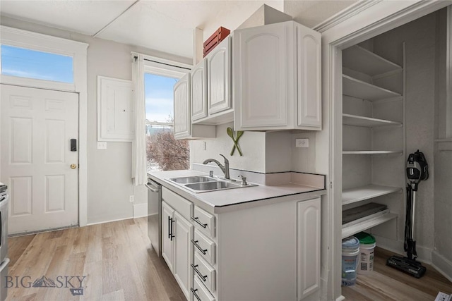kitchen with dishwasher, light countertops, light wood-type flooring, white cabinetry, and a sink