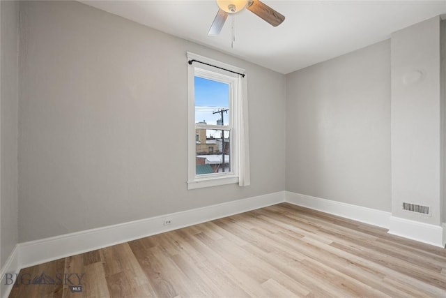 empty room with light wood finished floors, a ceiling fan, visible vents, and baseboards