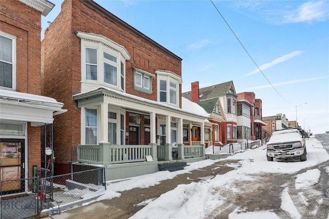 snow covered property with covered porch, fence, and brick siding