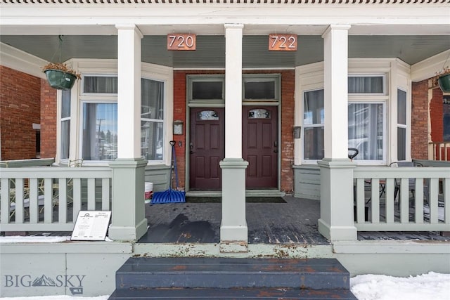 view of exterior entry featuring covered porch and brick siding