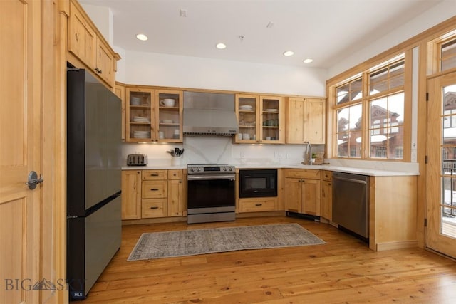 kitchen featuring wall chimney exhaust hood, appliances with stainless steel finishes, light wood-type flooring, and light countertops