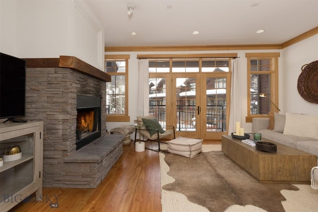 living area with a stone fireplace, recessed lighting, ornamental molding, french doors, and hardwood / wood-style floors