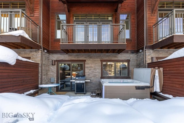 snow covered house featuring stone siding, a balcony, and a hot tub