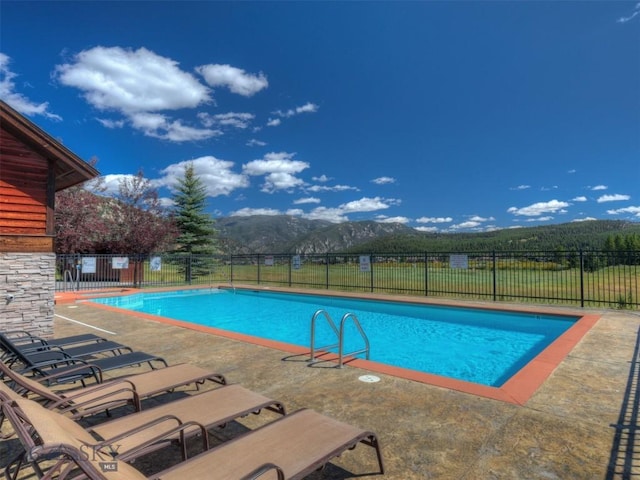 community pool with a patio, fence, and a mountain view