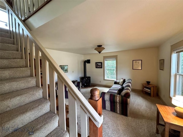 carpeted living area featuring stairs, a wealth of natural light, a wood stove, and baseboards