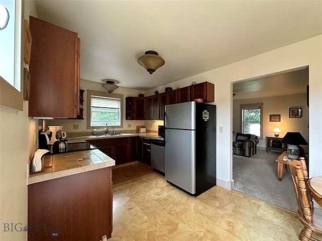 kitchen featuring light carpet, a sink, baseboards, appliances with stainless steel finishes, and tile counters