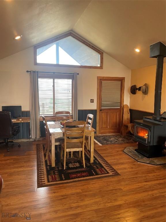 dining room with a wood stove, a wainscoted wall, vaulted ceiling, and wood finished floors