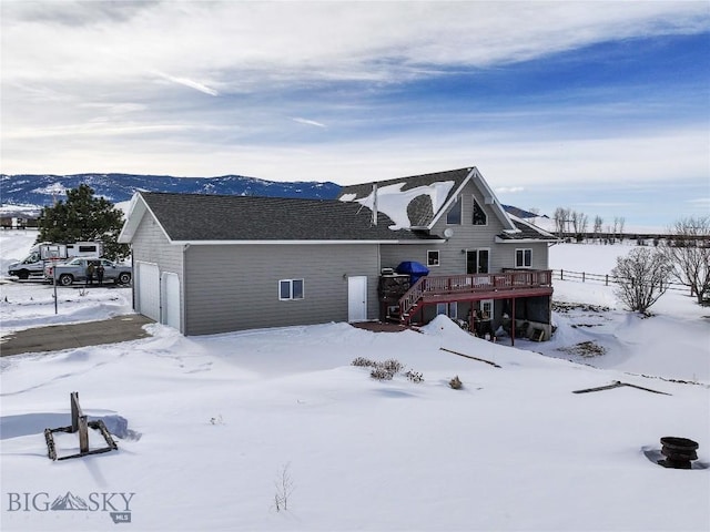 snow covered rear of property featuring a garage, an outdoor structure, a wooden deck, and stairs