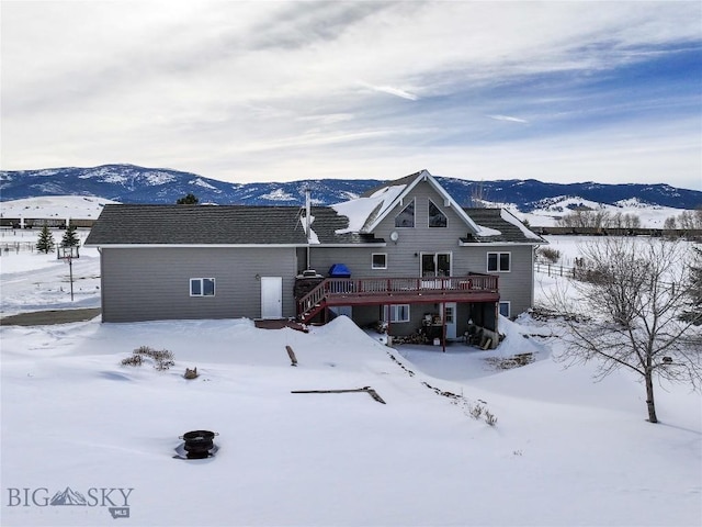 snow covered house with a deck with mountain view and stairway