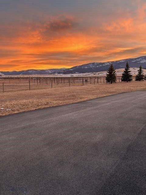 yard at dusk featuring a rural view, fence, and a mountain view