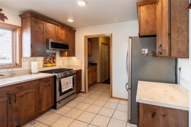 kitchen featuring a sink, light countertops, appliances with stainless steel finishes, decorative backsplash, and brown cabinetry