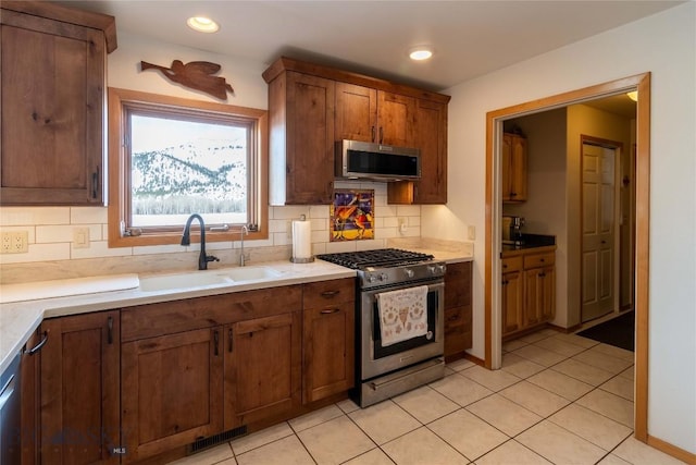 kitchen with appliances with stainless steel finishes, backsplash, light tile patterned flooring, and a sink