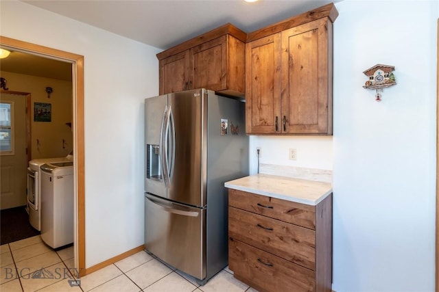 kitchen with light tile patterned flooring, light countertops, brown cabinetry, washer and clothes dryer, and stainless steel fridge