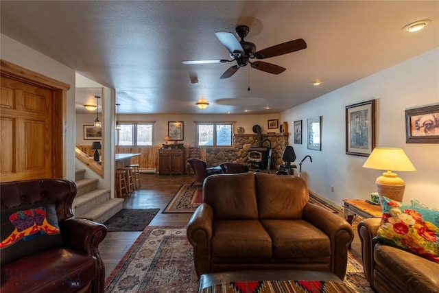 living area with dark wood-style floors, baseboard heating, a ceiling fan, a wood stove, and stairs