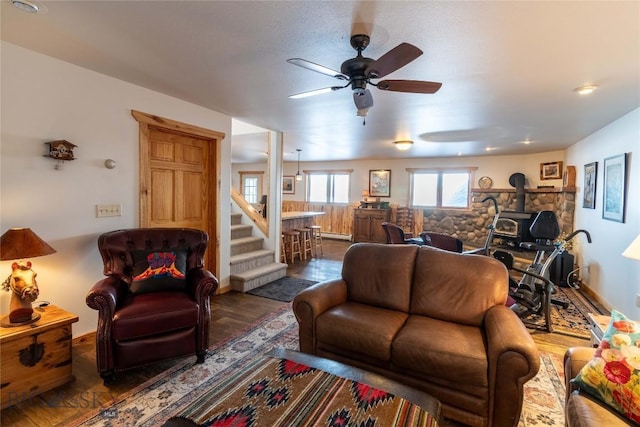 living area featuring a wood stove, stairs, a ceiling fan, and wood finished floors