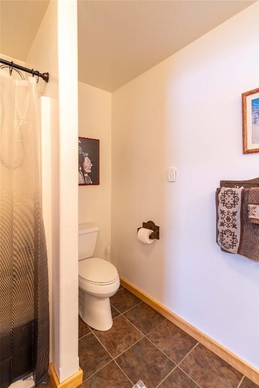 bathroom featuring toilet, tile patterned flooring, baseboards, and a shower with shower curtain