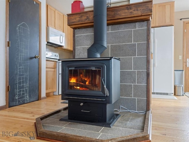 interior details with a wood stove, white appliances, and wood finished floors