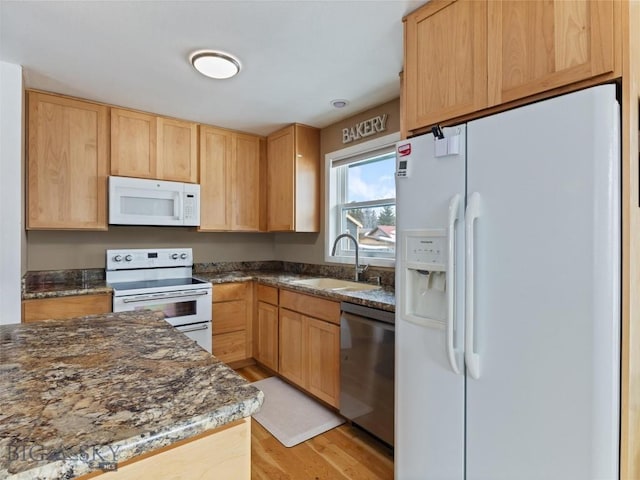 kitchen featuring light brown cabinetry, white appliances, a sink, dark stone countertops, and light wood-style floors
