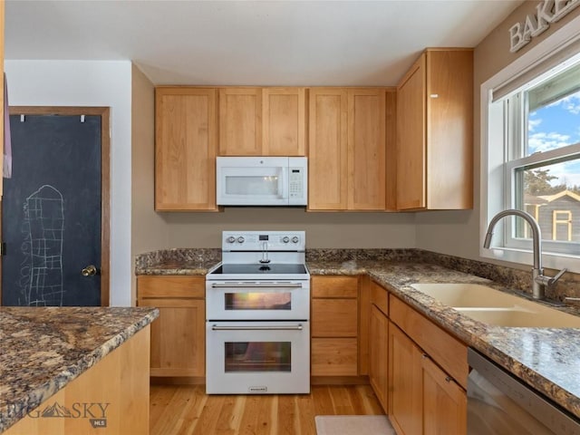 kitchen with a sink, light wood finished floors, white appliances, and dark stone countertops
