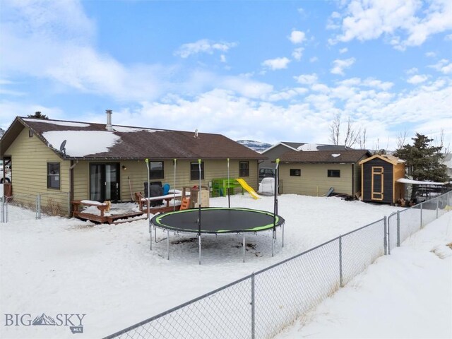 snow covered rear of property with a trampoline, an outbuilding, a fenced backyard, and a shed