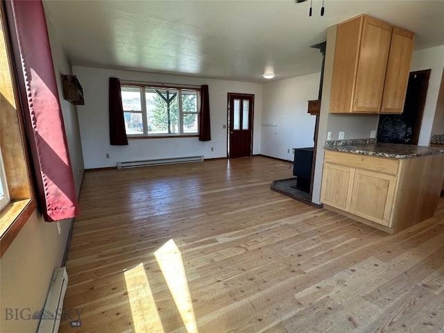 interior space featuring a baseboard heating unit, light wood-style flooring, open floor plan, light brown cabinets, and dark countertops