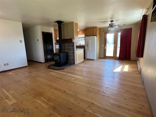 unfurnished living room featuring a wood stove, baseboards, a ceiling fan, and light wood-style floors