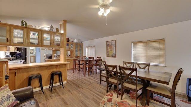 dining area with a ceiling fan, light wood-type flooring, and vaulted ceiling