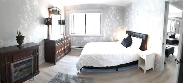 bedroom with light wood-type flooring, a fireplace, and baseboard heating