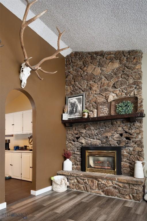 unfurnished living room featuring a fireplace, arched walkways, dark wood finished floors, and a textured ceiling