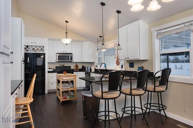 kitchen with a peninsula, white cabinets, black appliances, dark countertops, and dark wood finished floors