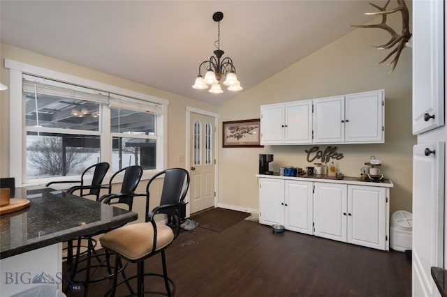 dining room with lofted ceiling, an inviting chandelier, baseboards, and dark wood-type flooring